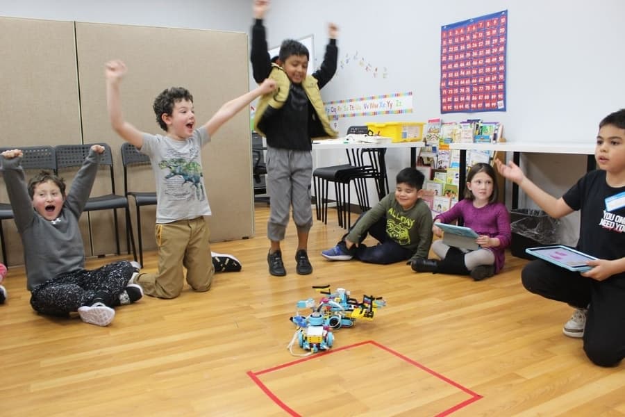Students cheering around a small robot during a STEM camp activity